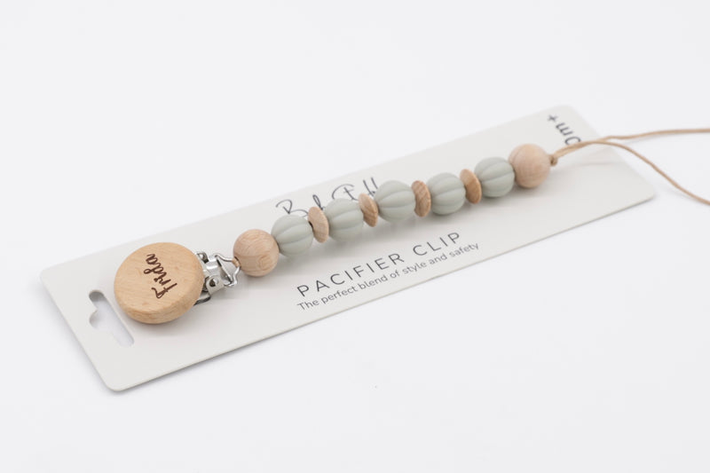 A handmade baby pacifier clip displayed flat on white packaging with "BabyStuff" branding. The clip features soft, cloud-grey silicone beads interspersed with natural wood-effect beads and a round wooden clasp