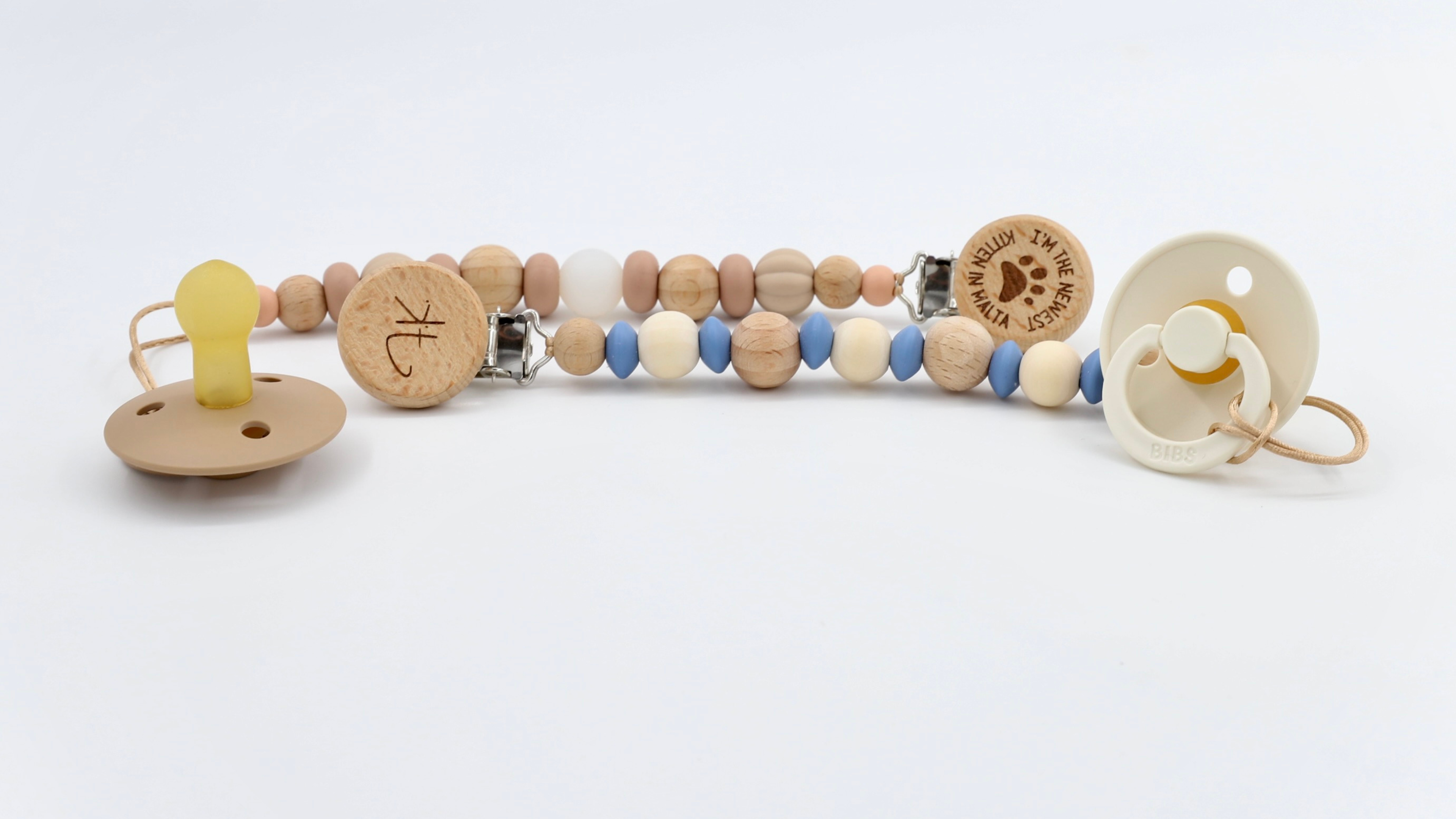 Two personalised BabyStuff dummy clips with engraved wooden beads, paired with BIBS dummies in soft neutral tones — Malta-based newborn gift item.