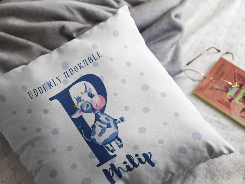 Mosaic Cow Cushion design with slogan "Udderly Adorable" and personalised baby name on a bed
